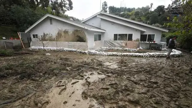 Mud and storm runoff across the yard of a sandbagged home below a hillside